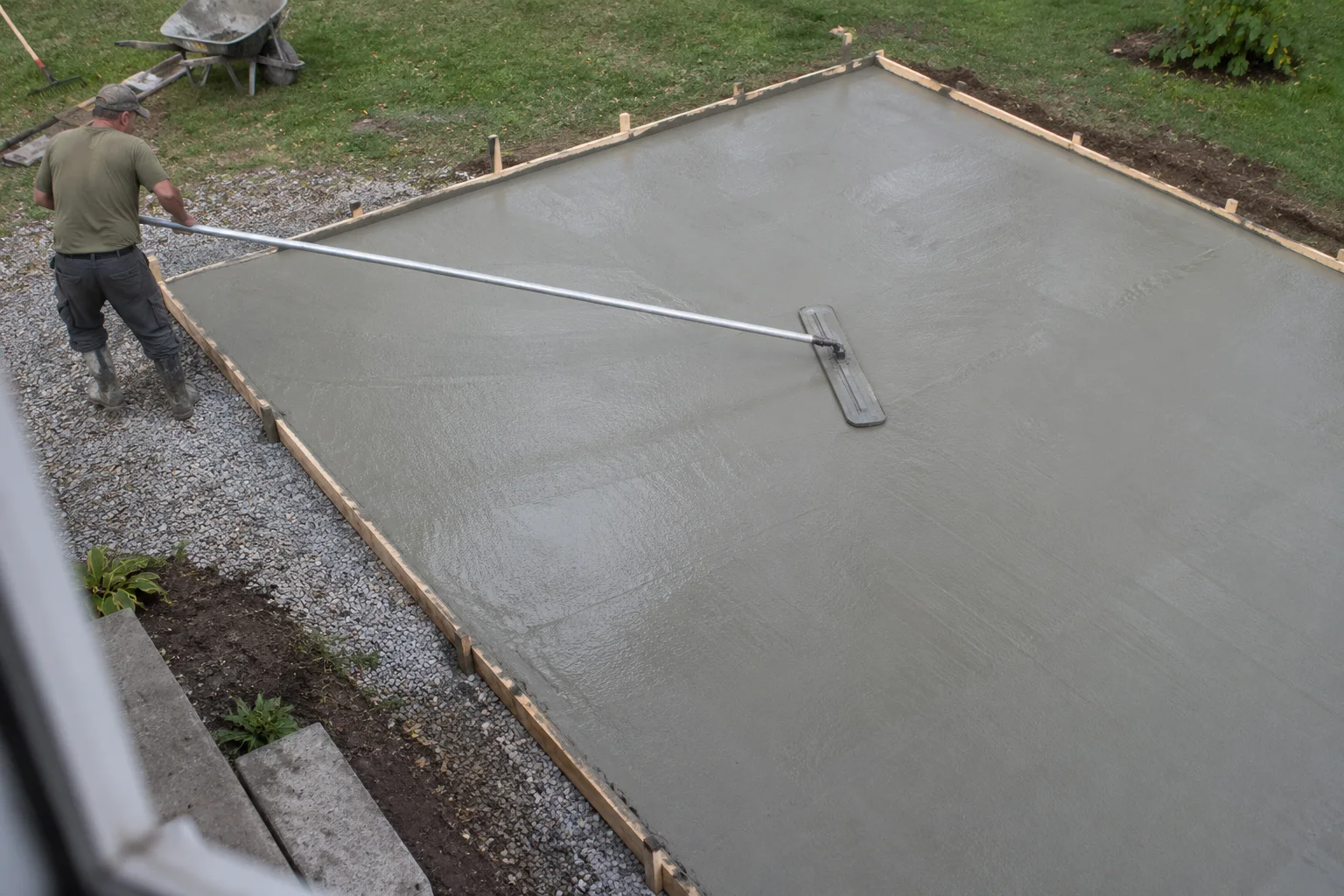 Worker seen from above smoothing a backyard concrete patio with a long-handled bull float